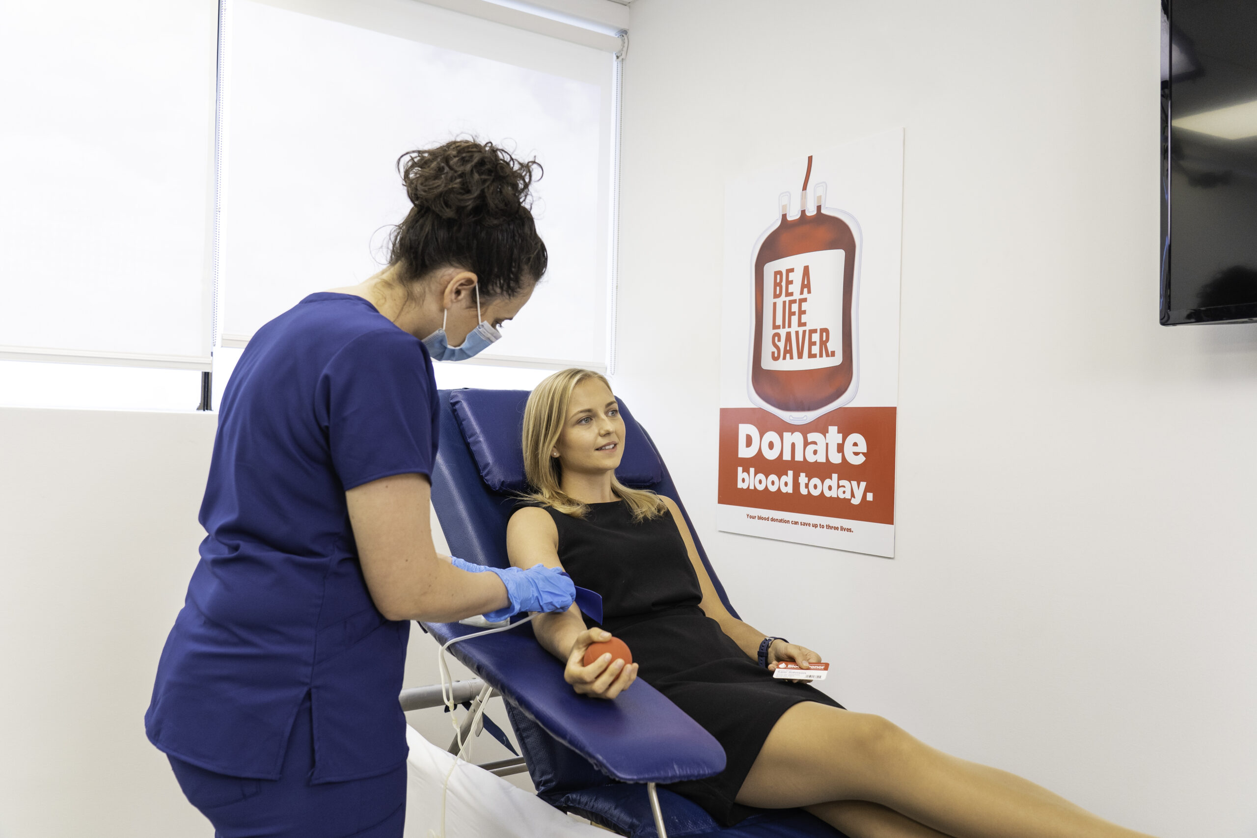 Blood donor with phlebotomist in front of sign reading Donate Blood Today