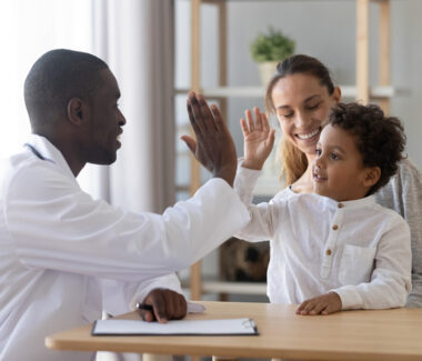 Doctor giving high five to child on his mother's lap.